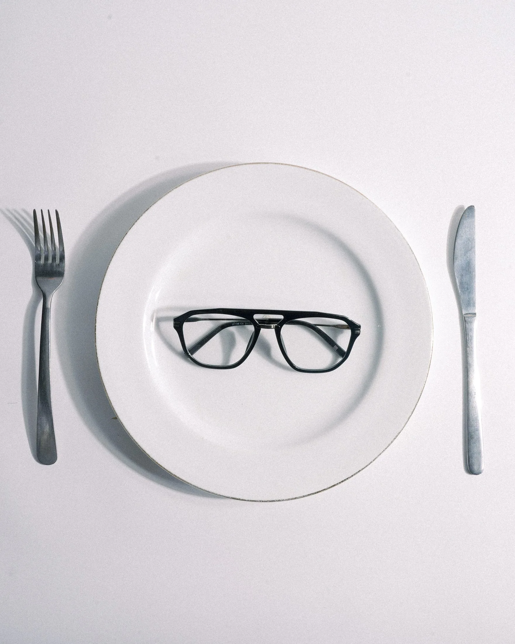 A pair of glasses served on a white plate with a fork and knife